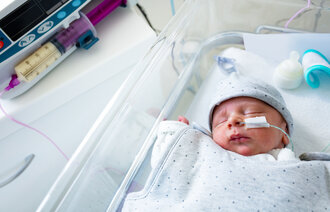 Bildet viser en baby i en sykehusseng. Den har sonde i nesten, og en sprøyte med morsmelk ligger ved siden av