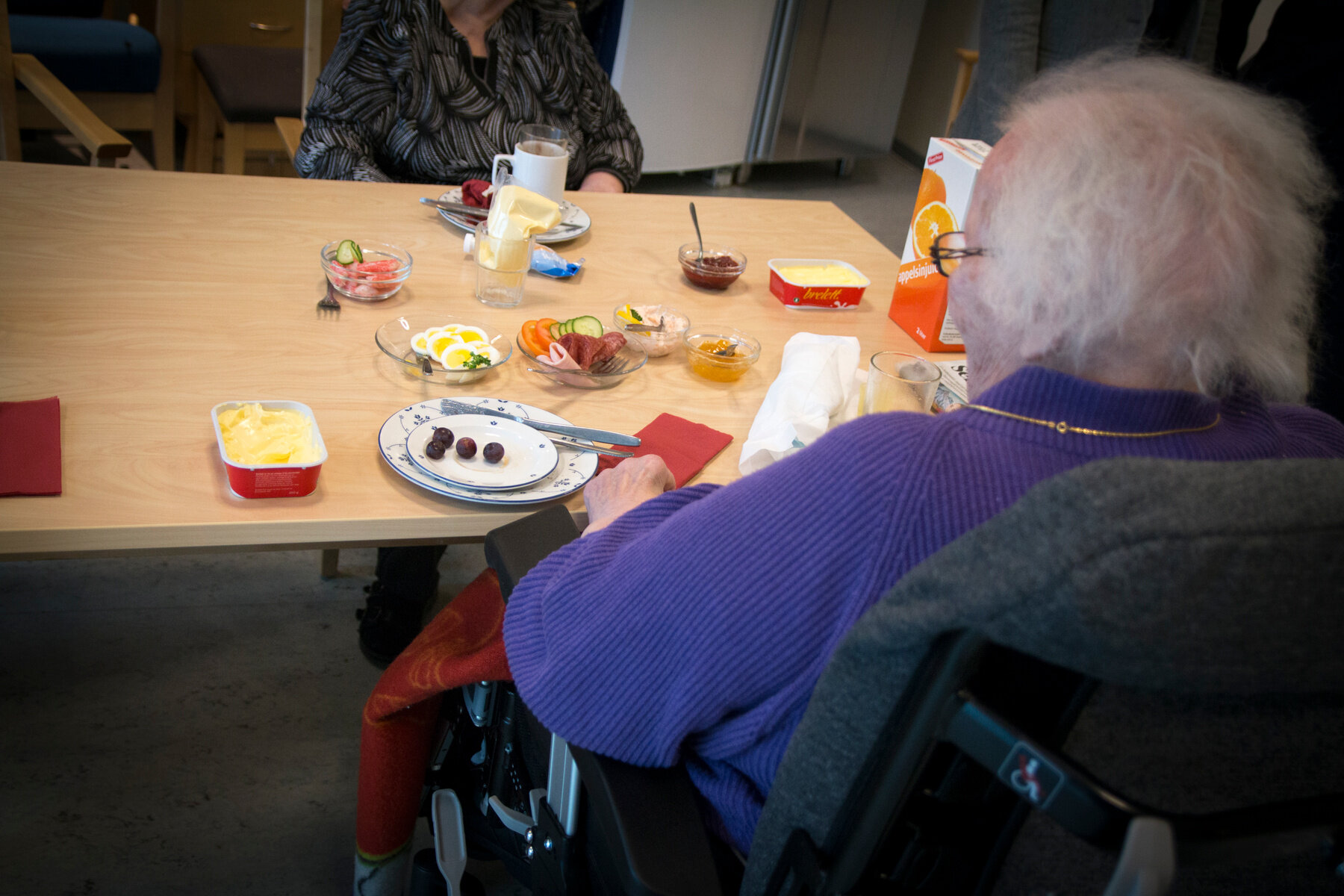 Bildet viser en eldre person som sitter og spiser mat med ryggen til