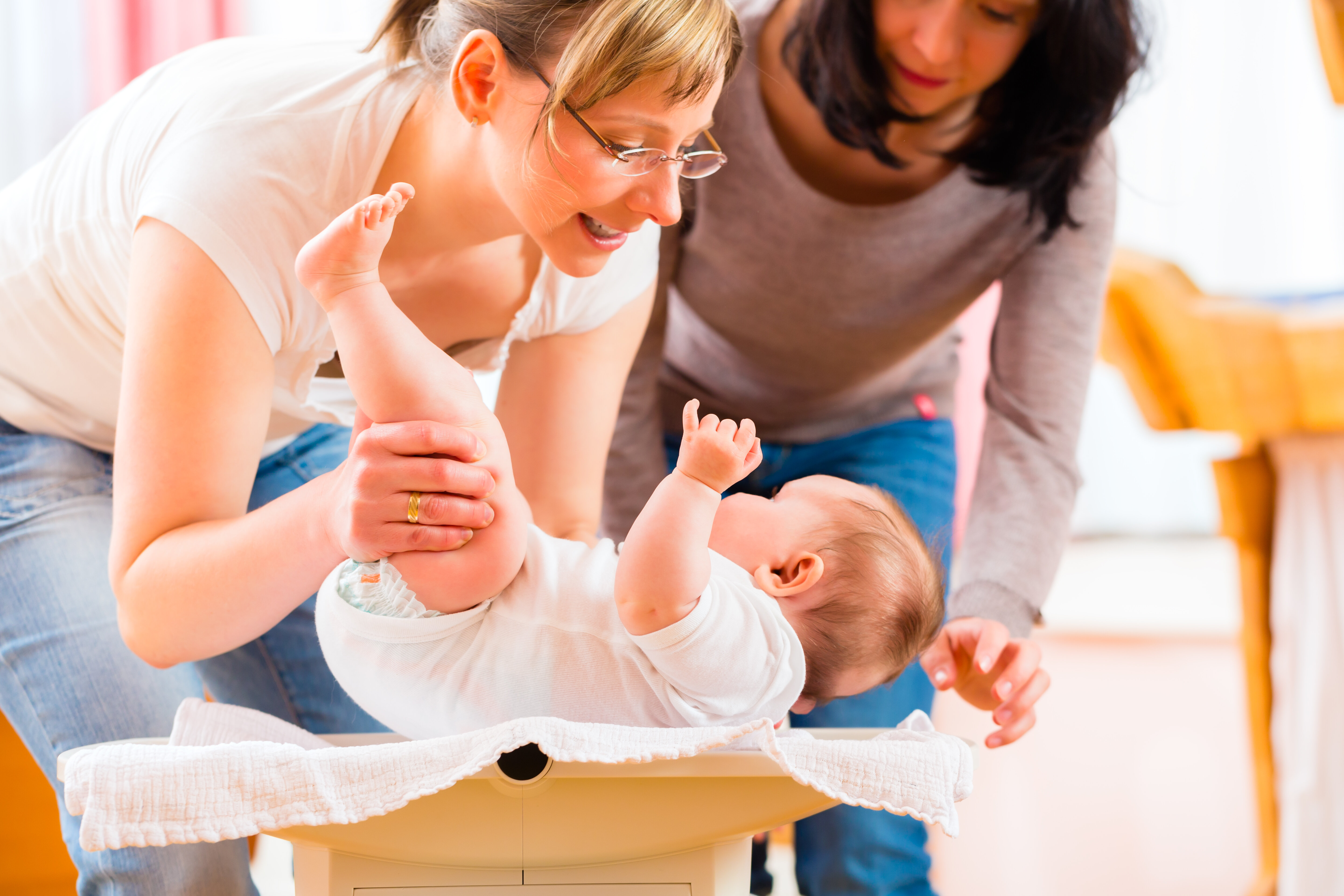 Bildet viser en helsesykepleier som veier en baby, mens moren står ved siden av