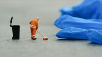 Bildet viser en miniatyrmann som koster opp rundt en engangshanske av plast