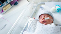 Bildet viser en baby i en sykehusseng. Den har sonde i nesten, og en sprøyte med morsmelk ligger ved siden av