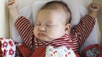 Baby som ligger i seng og strekker seg.