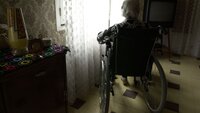 Sykehjemsbeboer i rullestol som sitter alene foran vindu