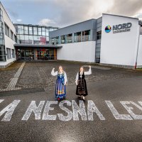 Bildet viser to bunadskledte mennesker utenfor høgskolen i Nesna, på bakken er det skrevet "La Nesna leve".