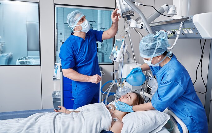 The photo shows two intensive care nurses standing by the bed of a patient being ventilated.